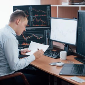 Reading the report. Man working online in the office with multiple computer screens in index charts.